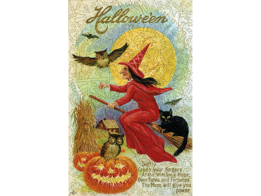 The front of the puzzle, Fates and Fortunes Halloween, showing a witch dressed in red, flying on a broomstick with a black cat, in front of a full moon. 